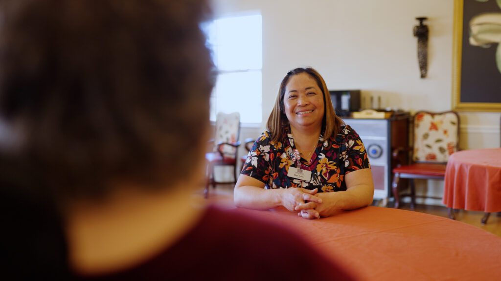 A nurse smiles at a resident in front of her in a skilled nursing facility